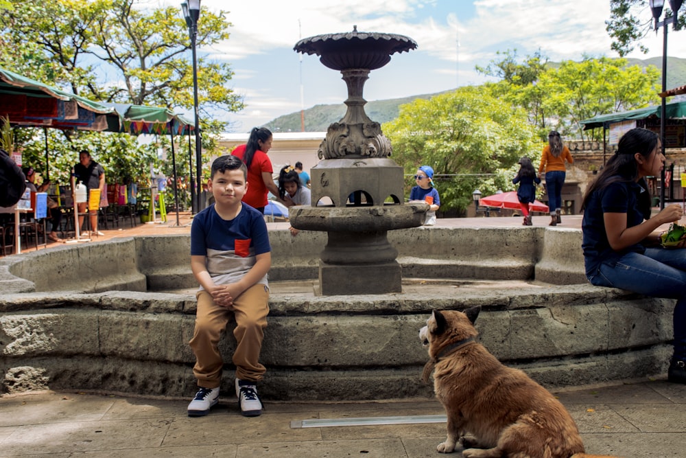 a boy and a dog sitting in front of a fountain