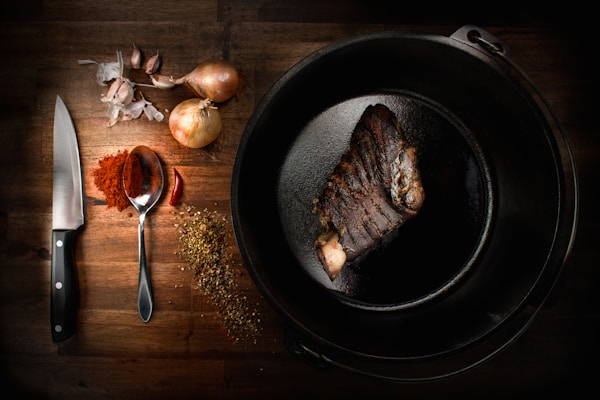 A steak is cooking in a skillet on a wooden table