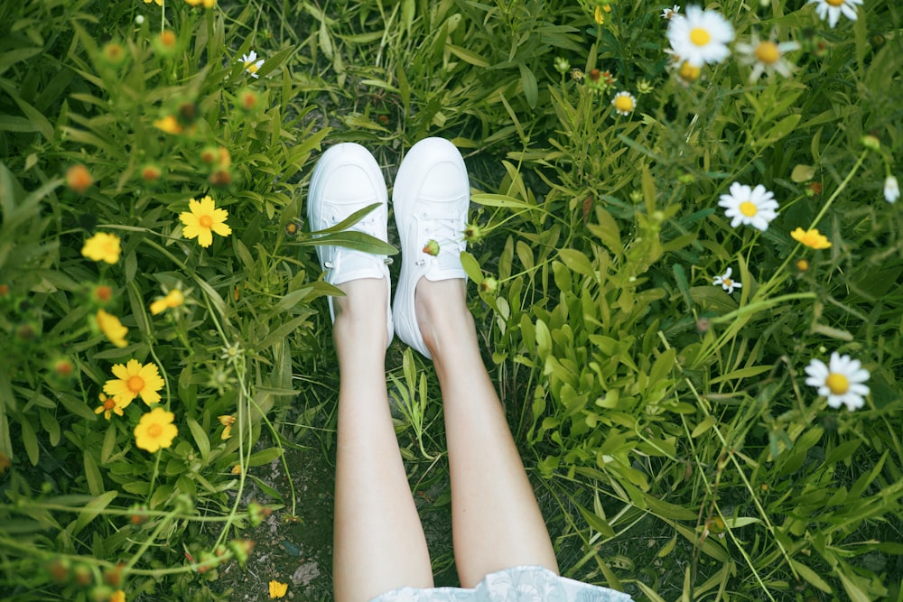 a person wearing white shoes standing in a field of flowers