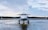 A private jet is parked on a wet runway, reflecting the overcast sky. The aircraft is positioned in the center, with a forest in the distance under a cloudy sky.