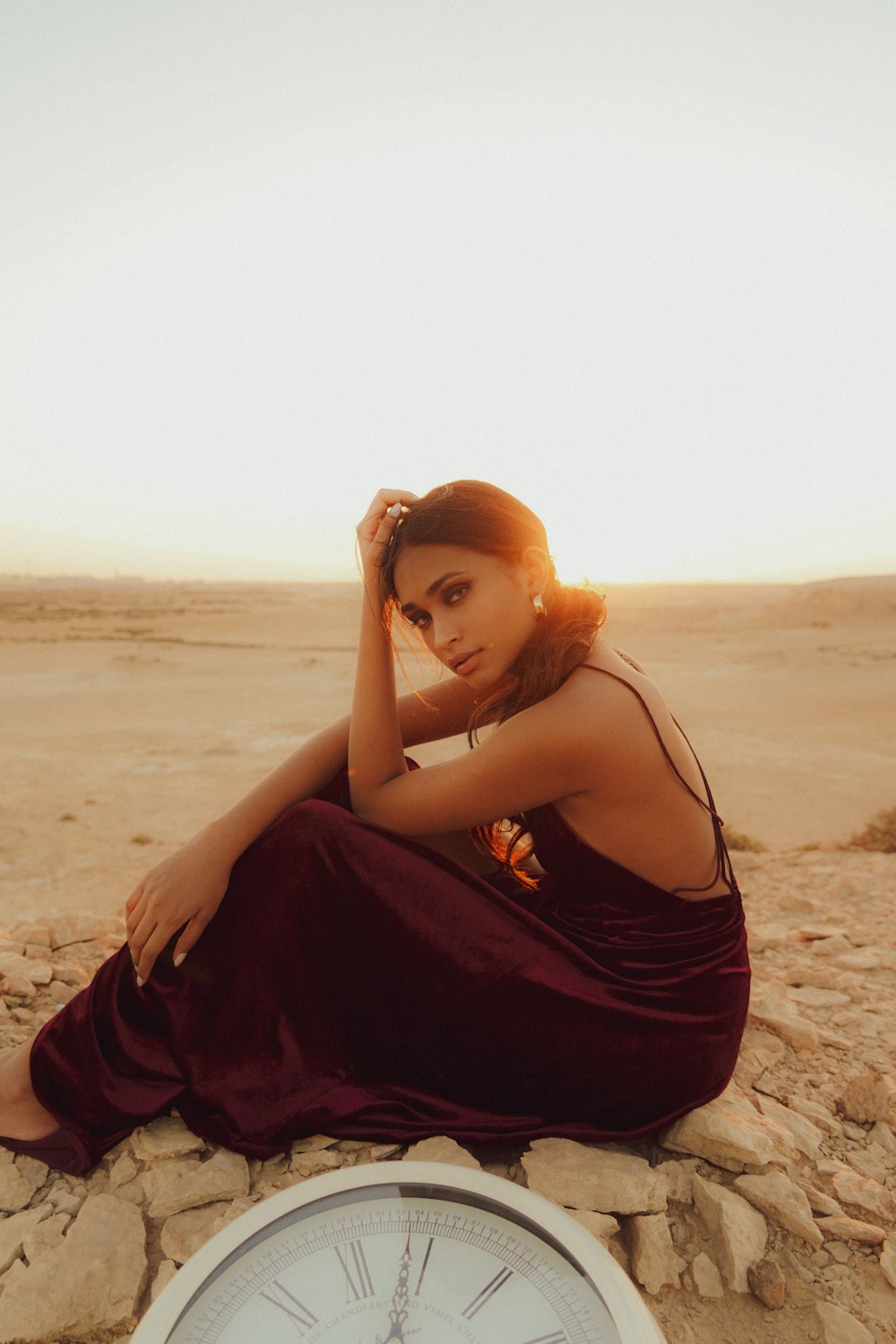 a woman sitting on top of a rock next to a clock