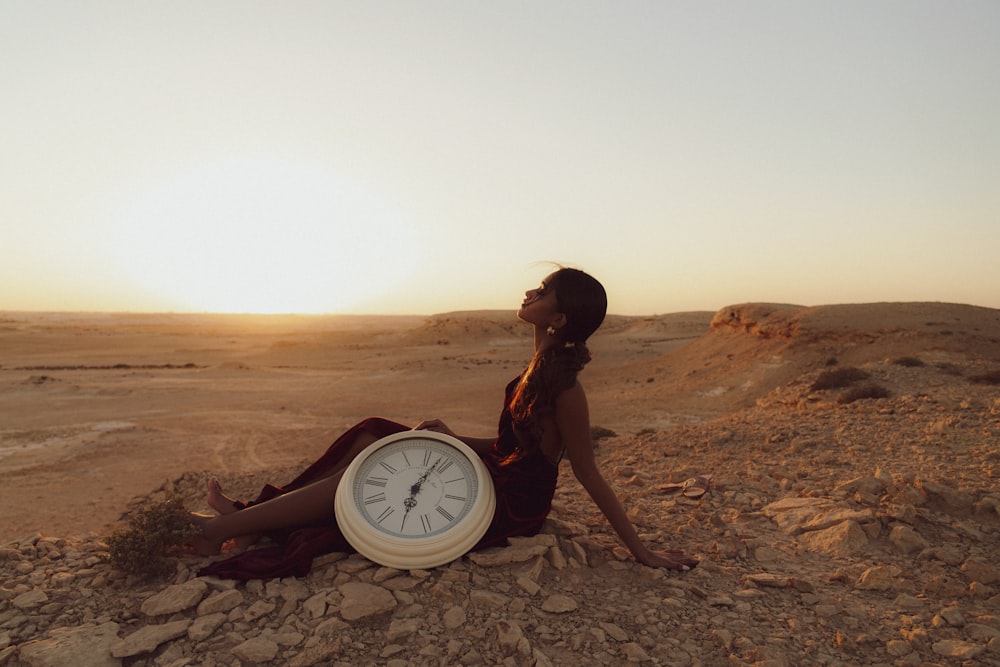 a woman sitting on the ground with a clock in front of her