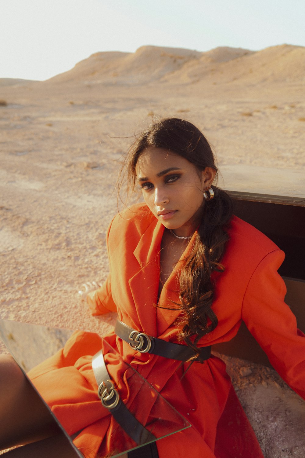 a girl in an orange dress sitting in the desert