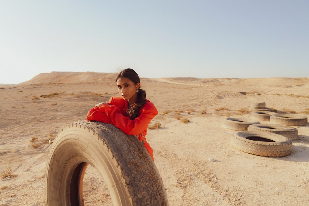 a woman sitting on top of a tire in the desert