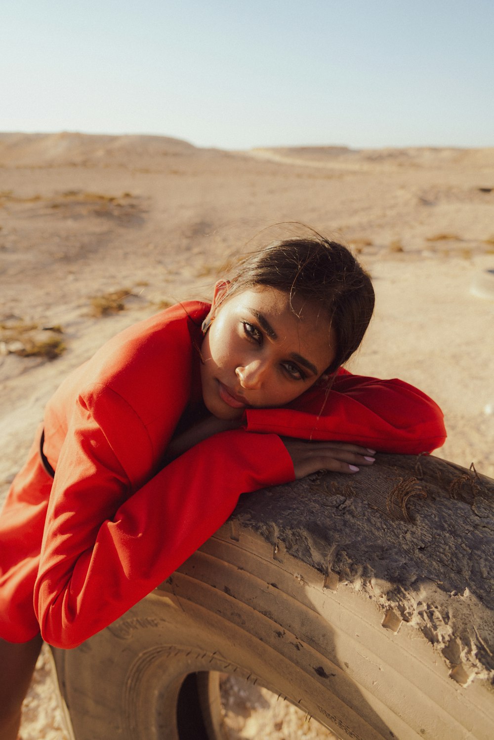 a woman in a red jacket leaning on a tire