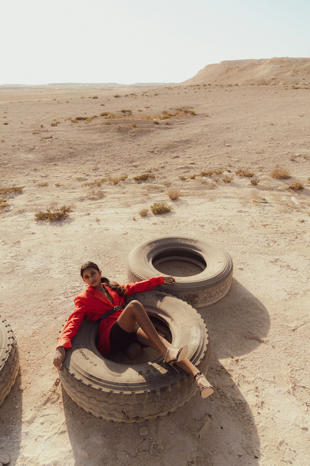 a woman sitting on top of a tire in the desert