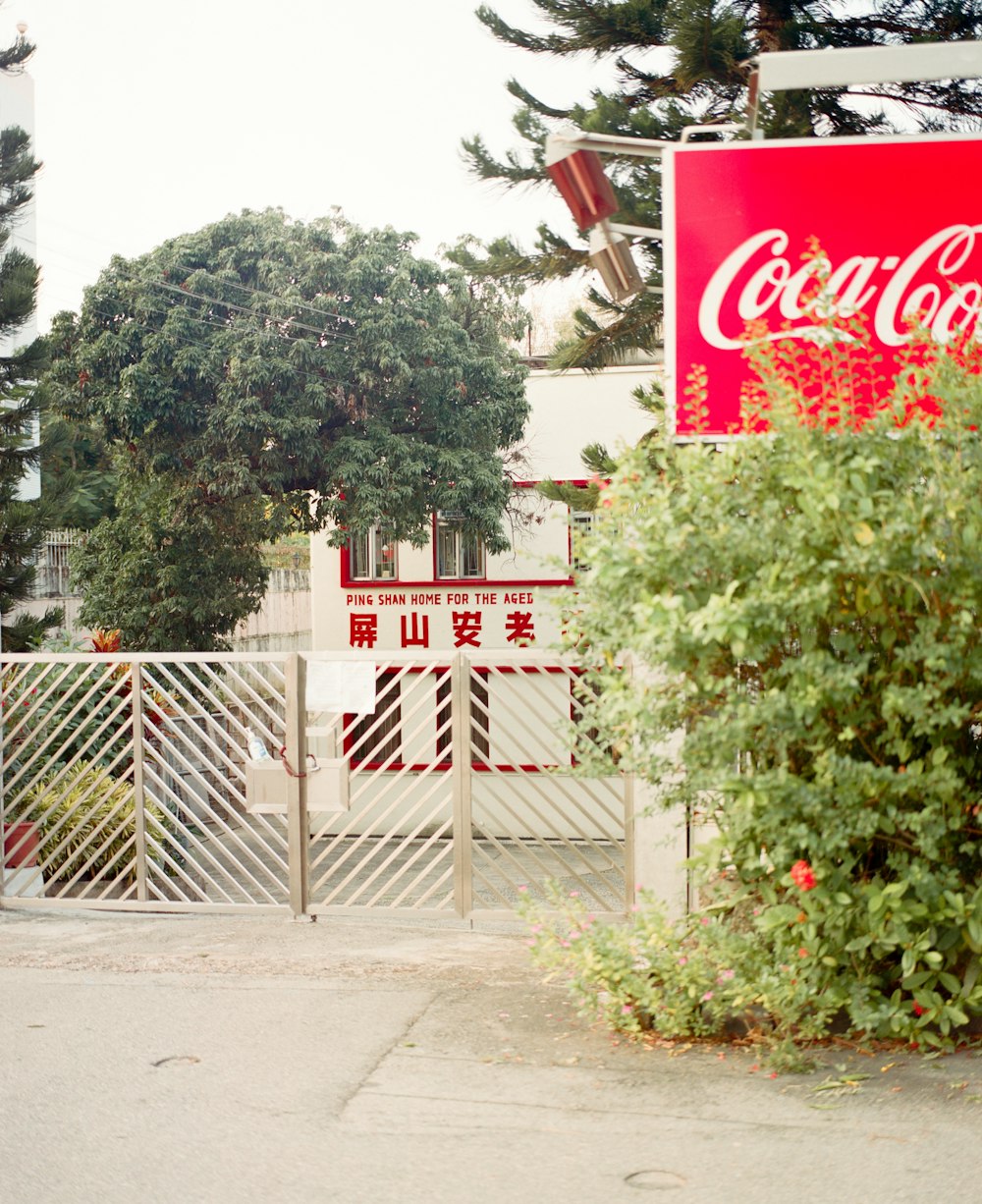 um sinal de coca - cola em uma cerca ao lado de um arbusto