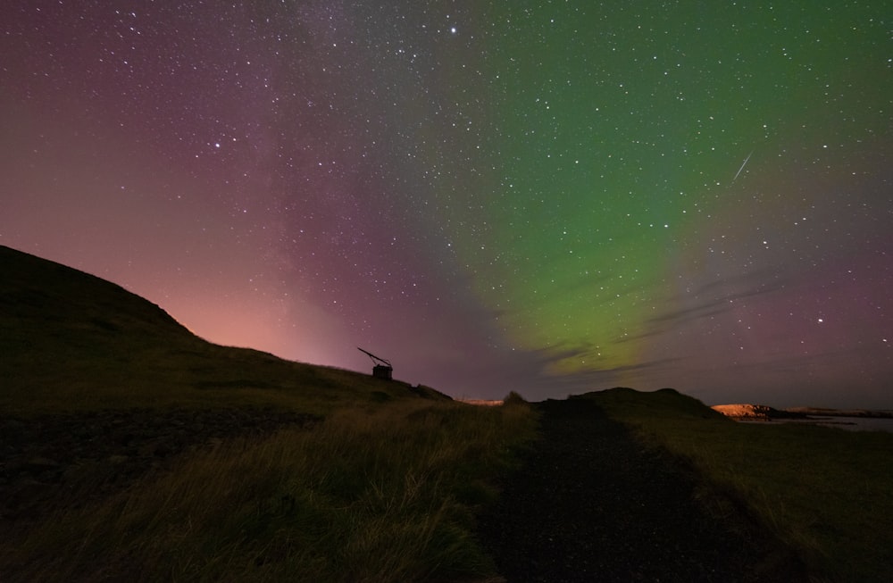 a green and purple aurora over a grassy hill