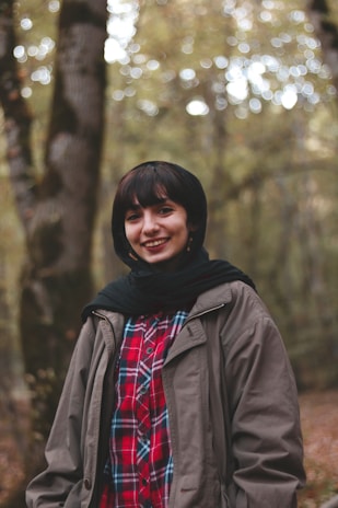 A close-up of a smiling traveler wearing warm clothes with the Tierra del Fuego forest behind.