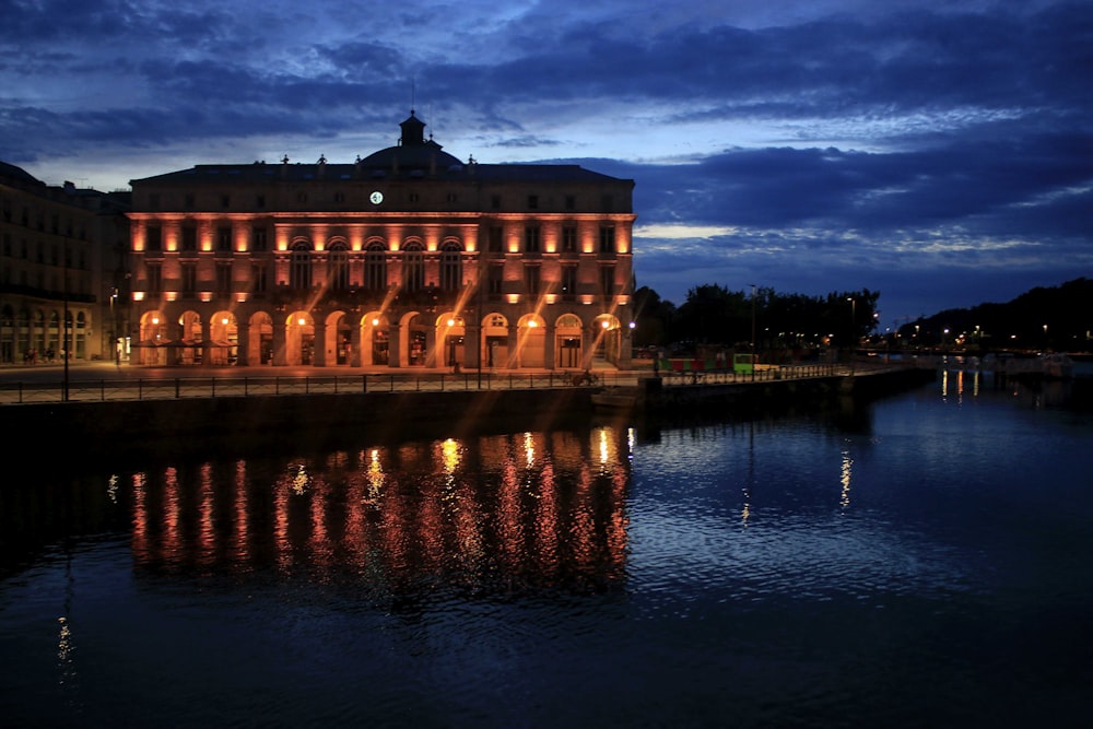 a building is lit up at night by a body of water