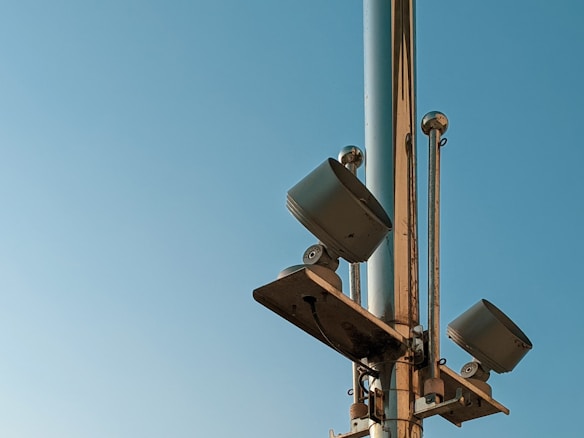 Metallic pole with mounted floodlights against a clear blue sky. Various rods and fixtures attach the lights to the structure.