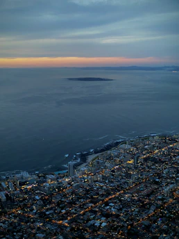 A sleek satellite view of a coastal city at dusk with teal and navy overlays highlighting geospatial data points.