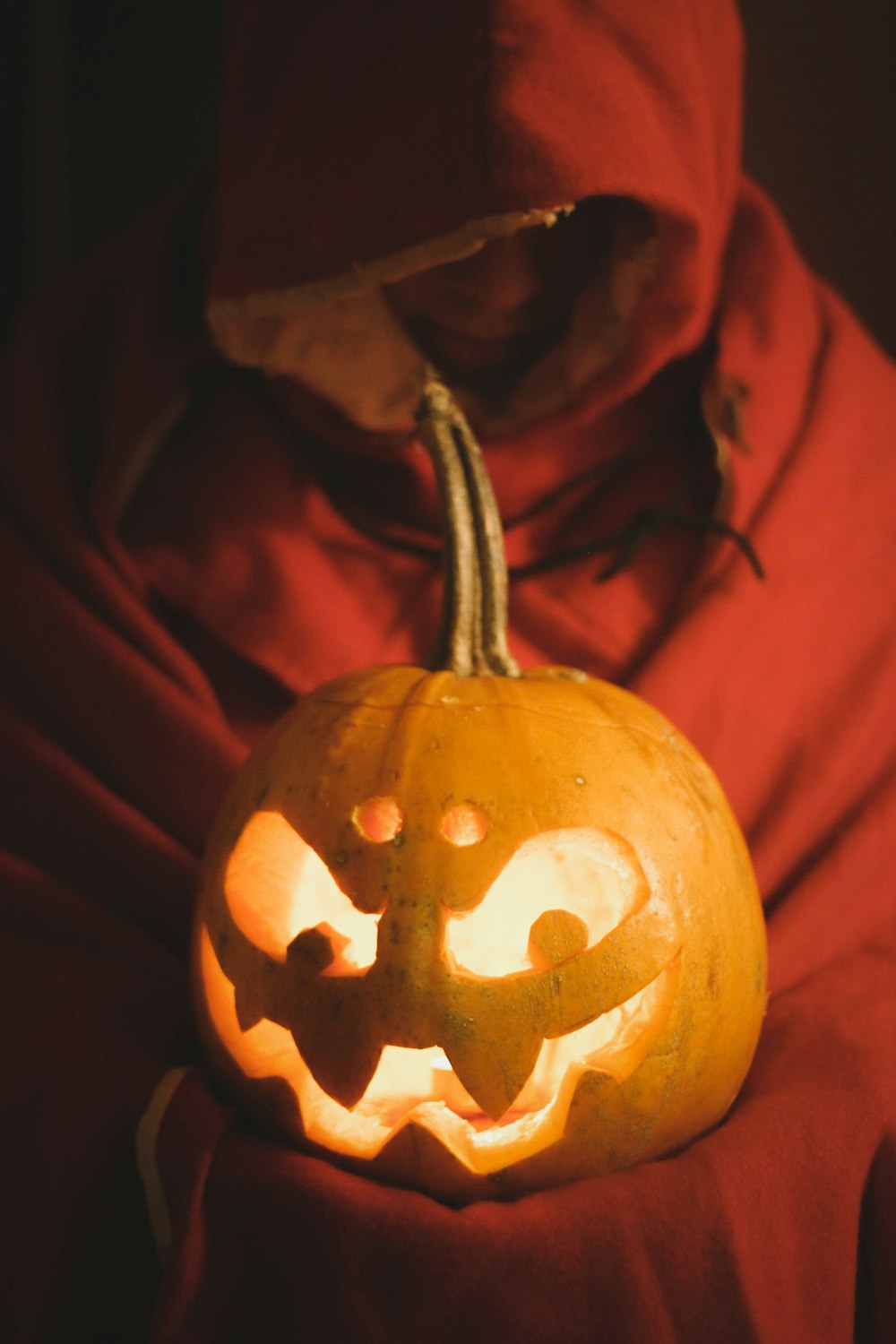 a person in a red hoodie holding a carved pumpkin