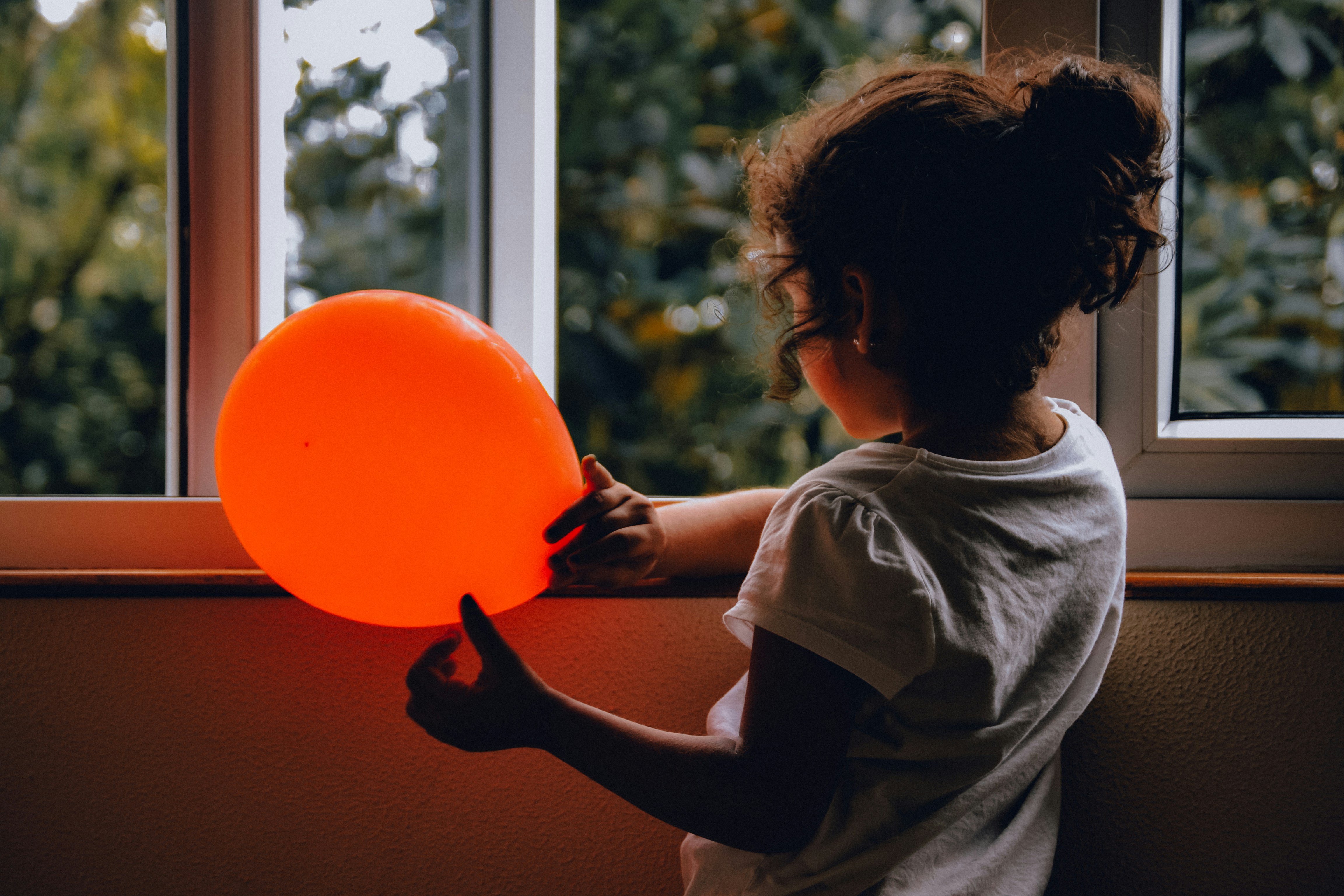 A child holding a glowing orange ball light by a window