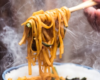 a person holding a wooden spoon full of noodles