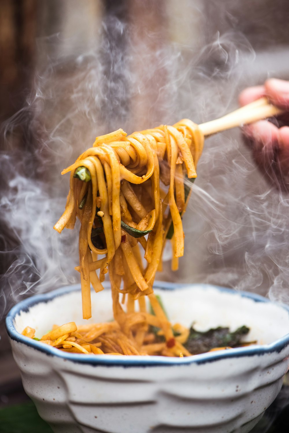 una persona sosteniendo una cuchara de madera llena de fideos