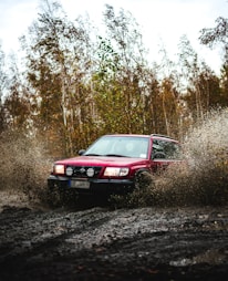 a red car driving through a puddle of mud