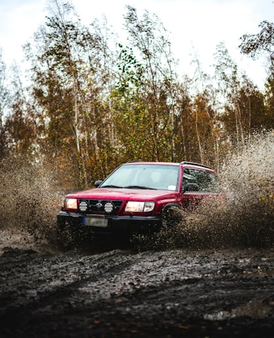 a red car driving through a puddle of mud