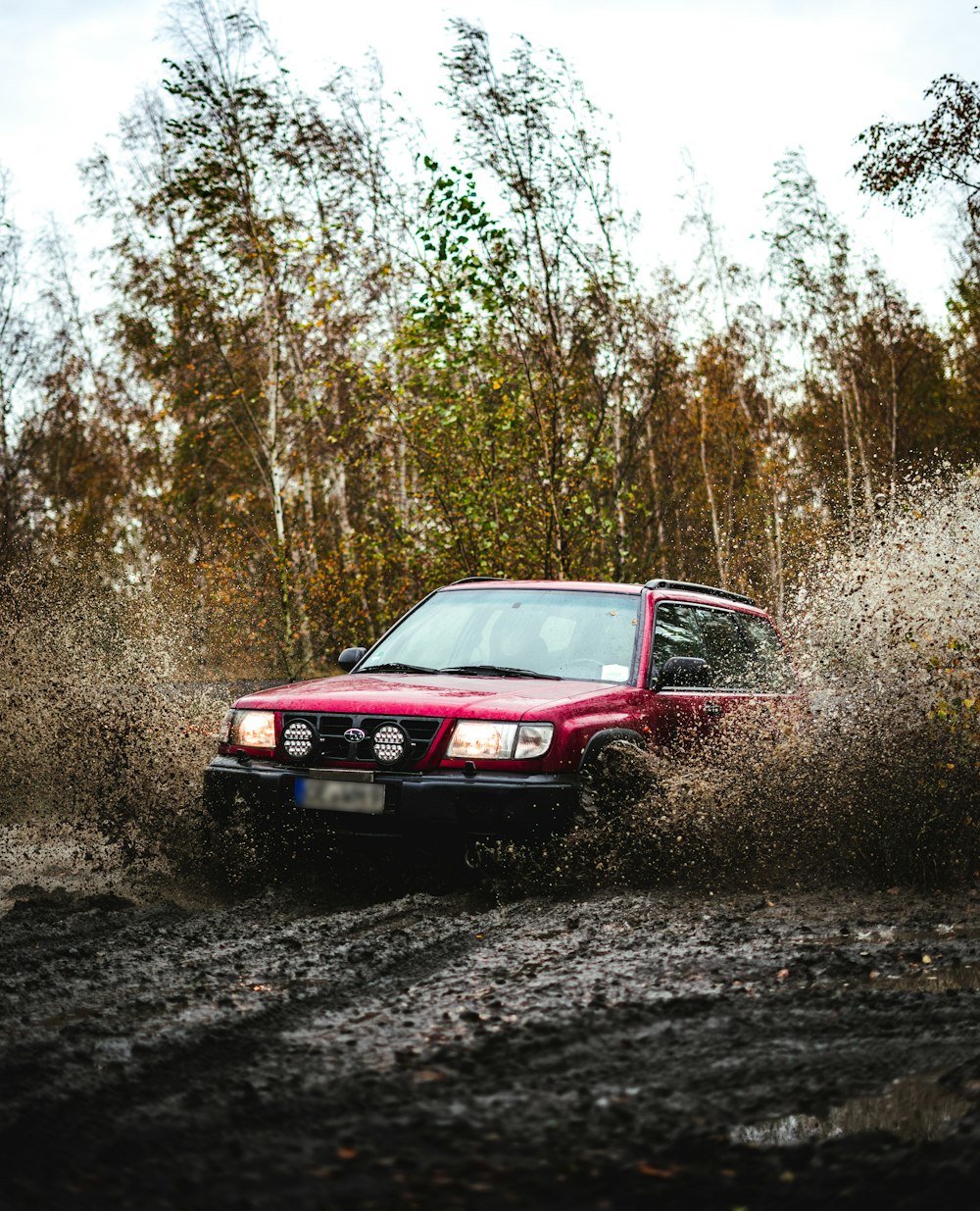 a red car driving through a puddle of mud