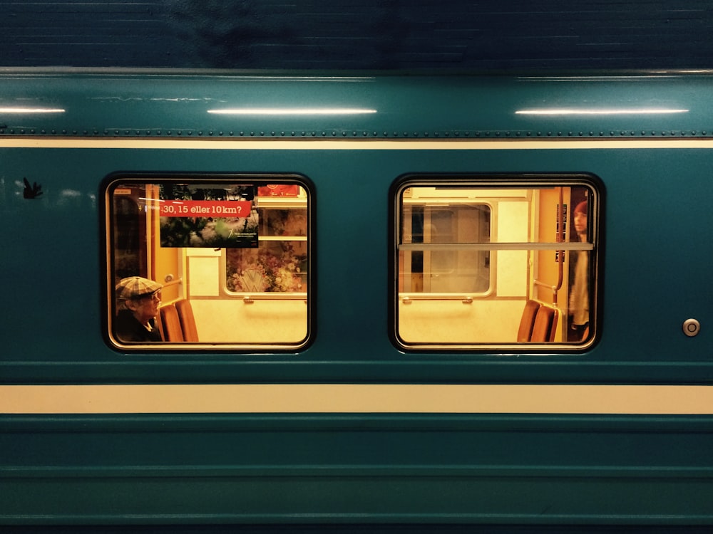 a green train car with two windows and a dog looking out the window