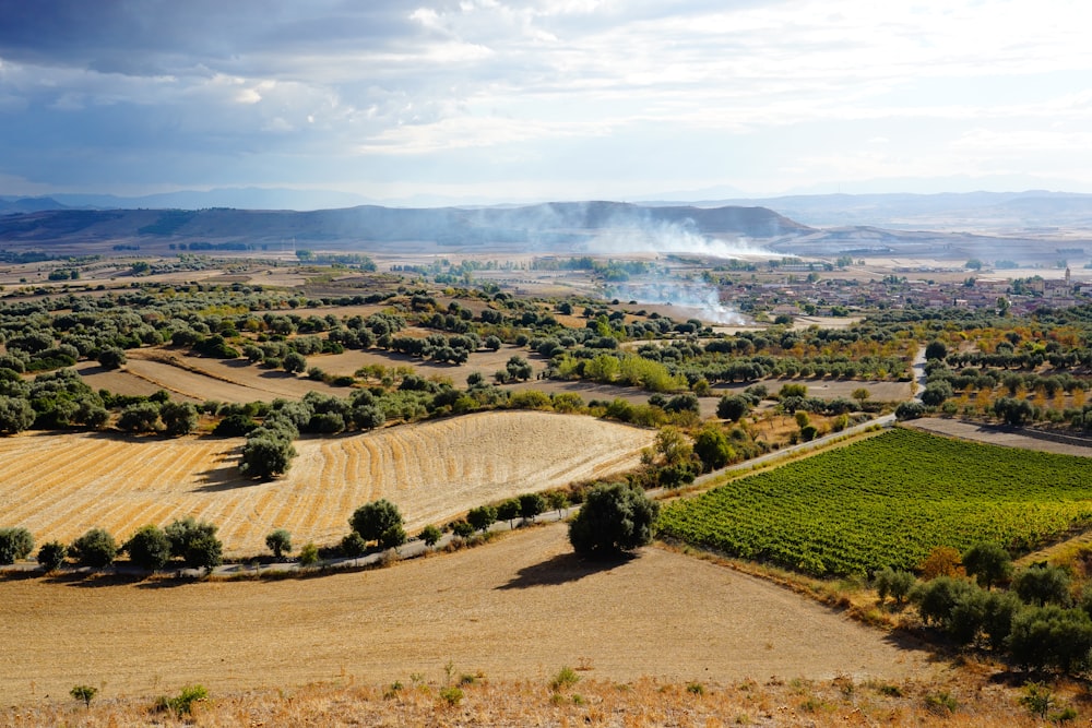 an aerial view of a farm land with smoke coming out of the distance