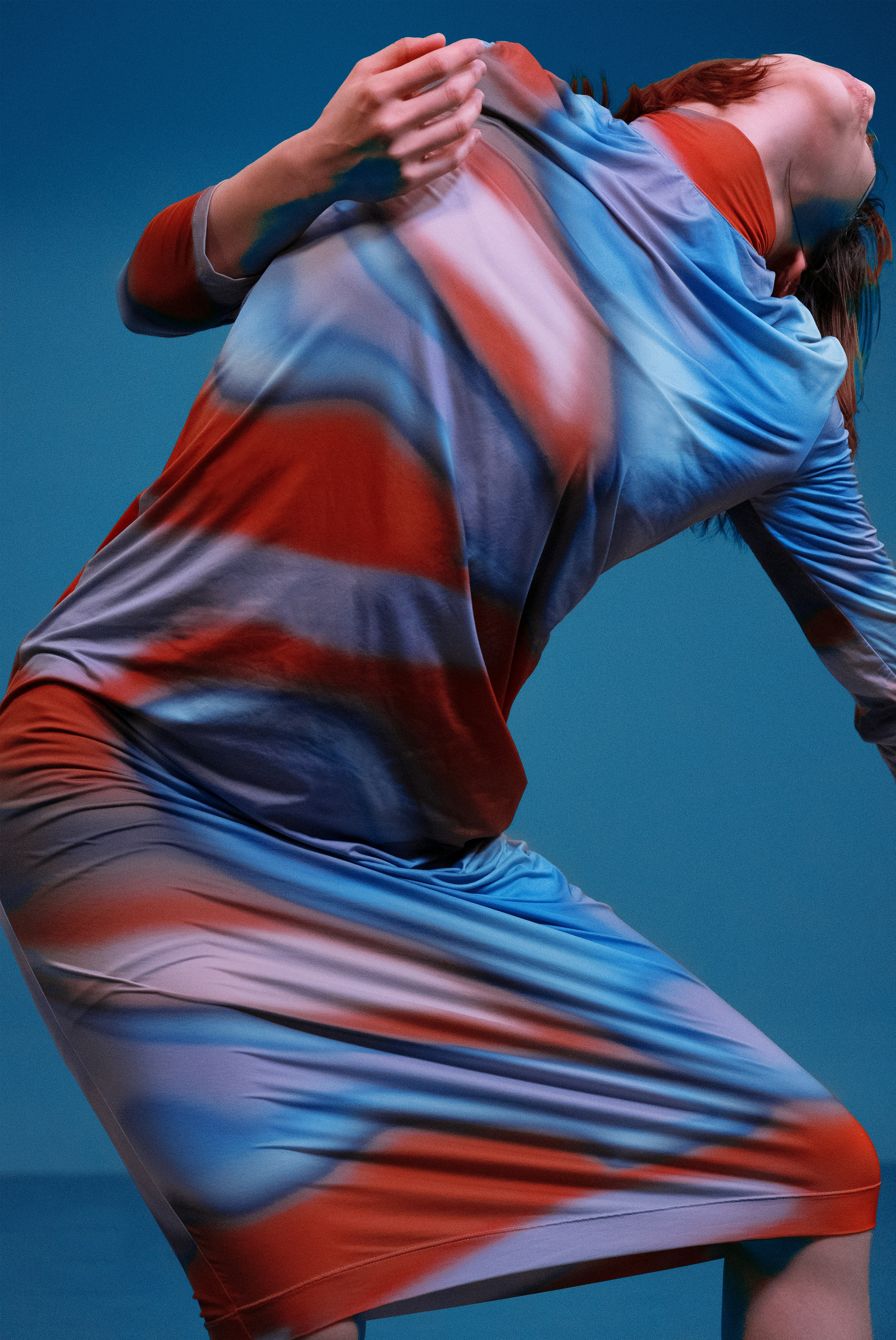 Woman in abstract gradient dress leans back with head tilted up.