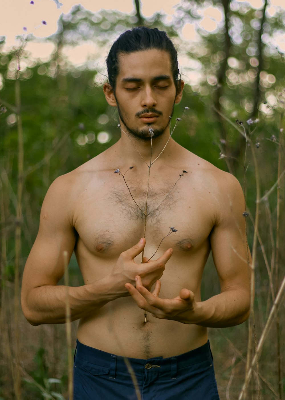 a shirtless man standing in a forest holding his hands together