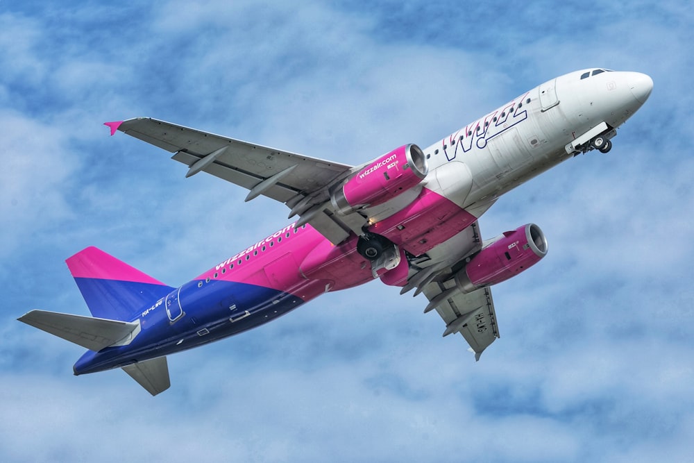 a pink and blue jet airliner flying in the sky