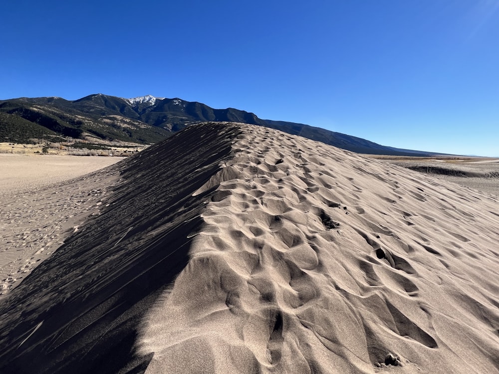a large sand dune with mountains in the background
