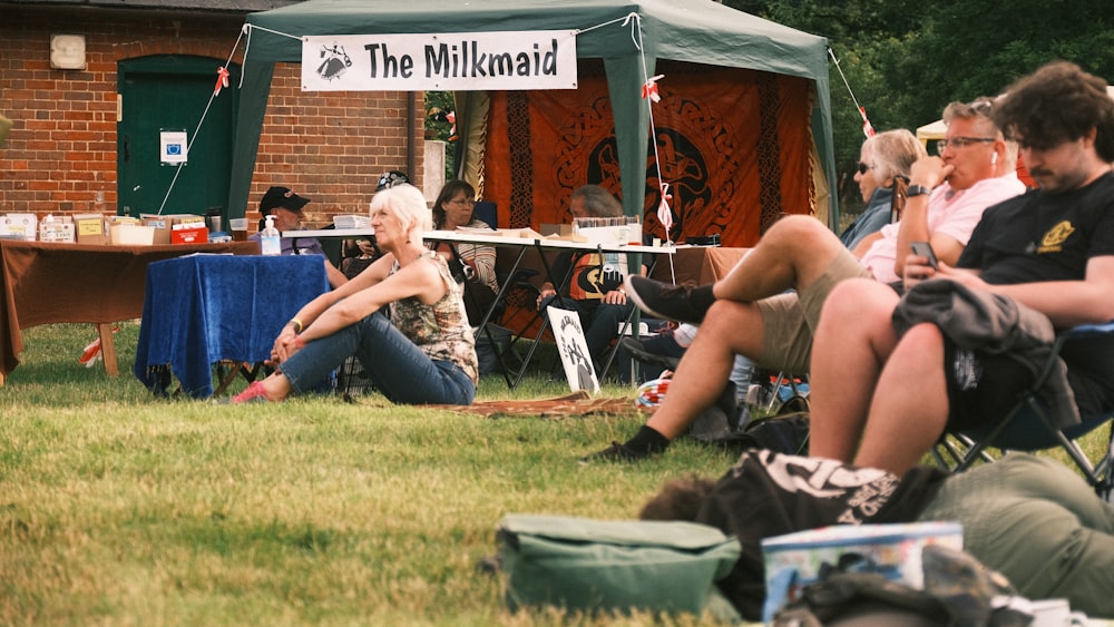 a group of people sitting in the grass under a tent