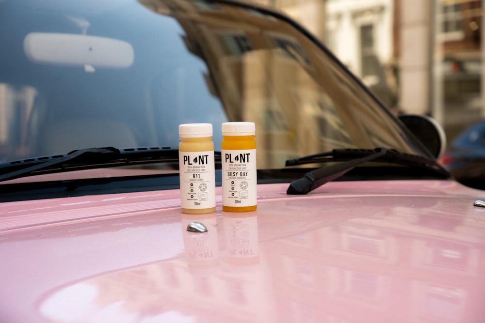 two bottles of paint sitting on top of a pink car