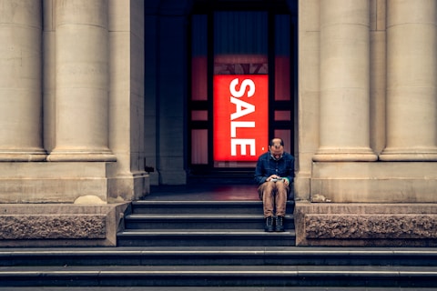 a man sitting on the steps of a building with a sale sign in the background
