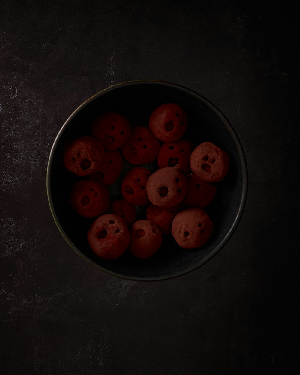 a bowl filled with red donuts on top of a table