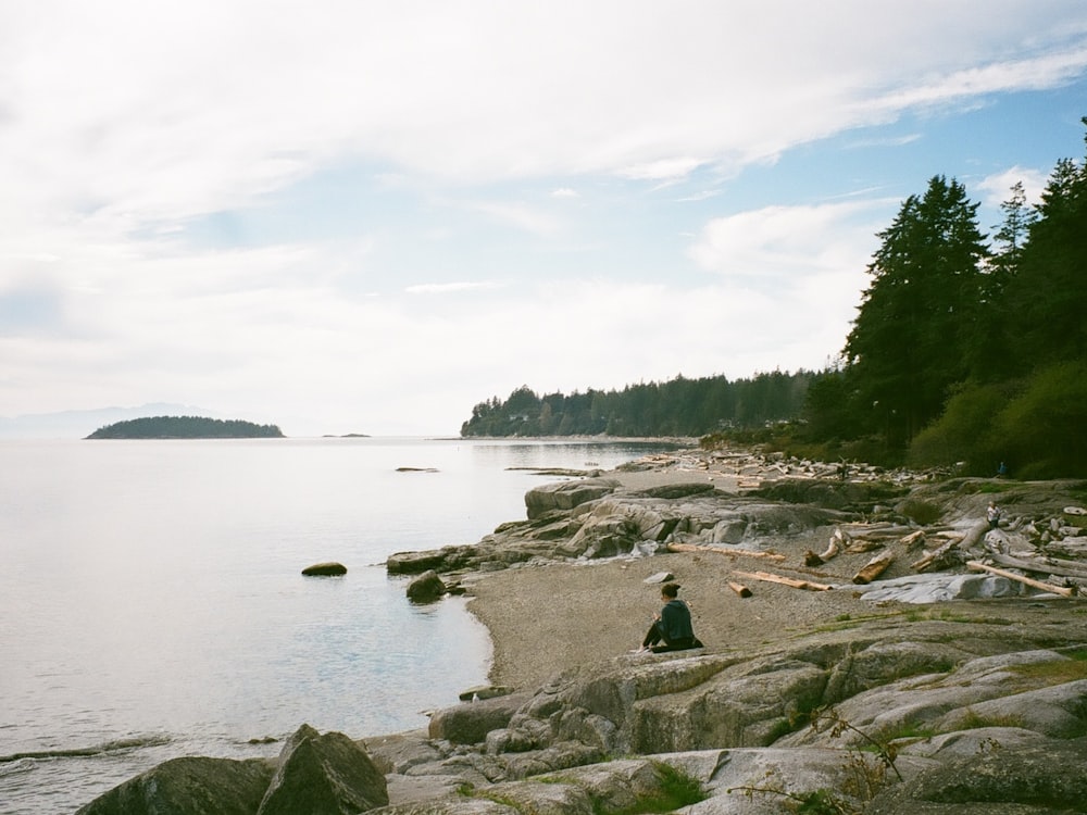 a person sitting on a rock near a body of water