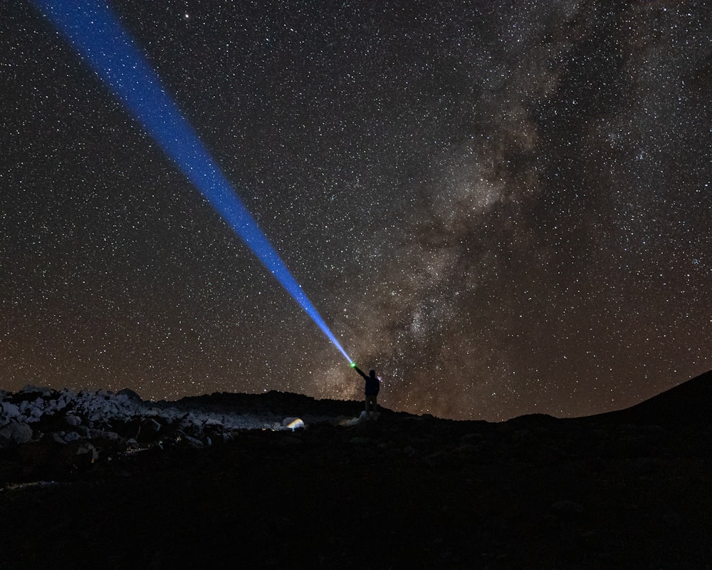 Un hombre parado en la cima de una montaña bajo un cielo lleno de estrellas