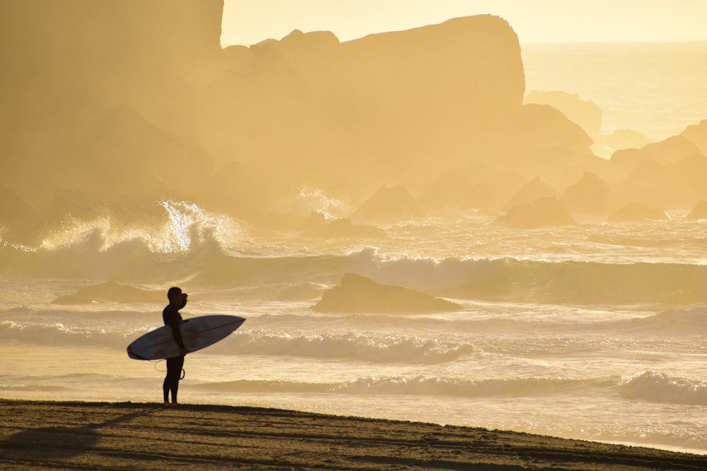 a person standing on a beach holding a surfboard