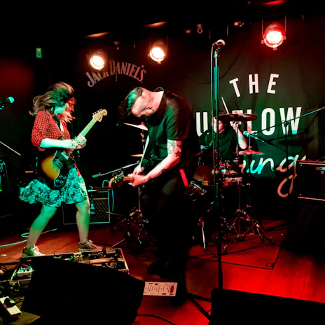 A candid shot of The Retellers passionately playing guitars on stage under warm amber lights.