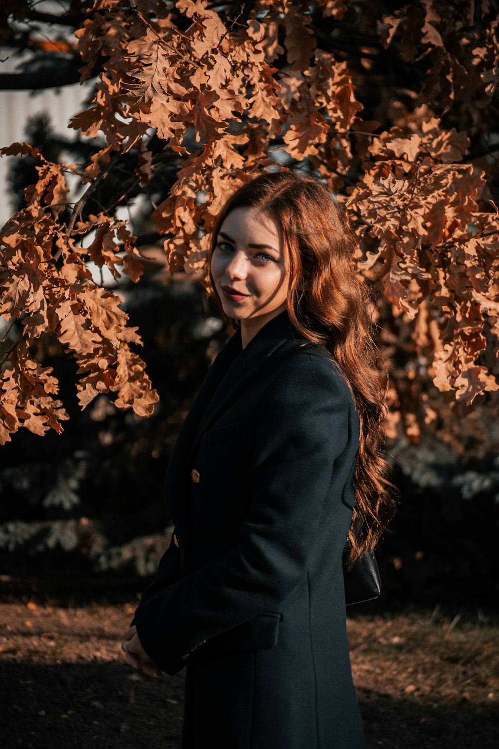 a woman in a black coat standing under a tree