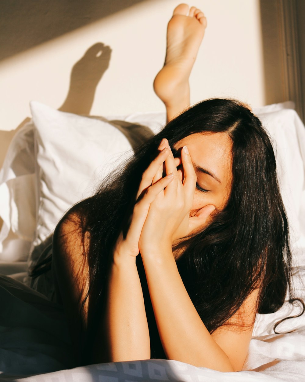 a woman laying in bed with her hands on her face