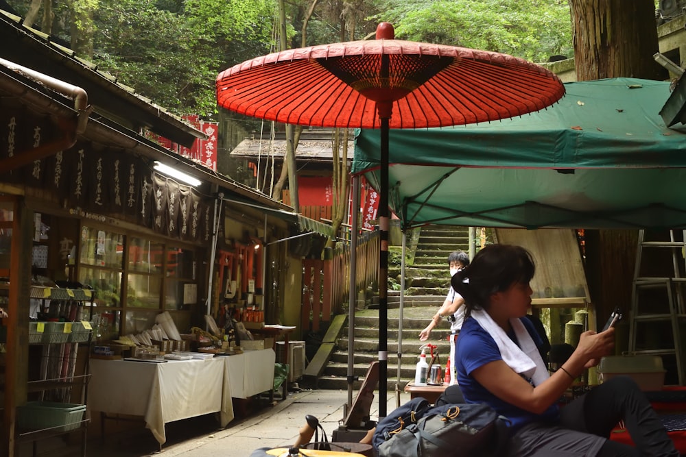 a woman sitting under an umbrella looking at her cell phone