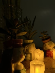 Several decorative ceramic planters shaped like faces with closed eyes, each containing a small plant, are arranged around glowing pillar candles. The setting has a dim, warm ambiance created by the candlelight.
