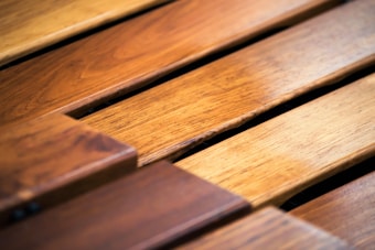 Close-up view of wooden planks displayed at an angle, highlighting their texture and grain patterns. The planks vary in shade from light to dark brown, suggesting a natural wood finish.