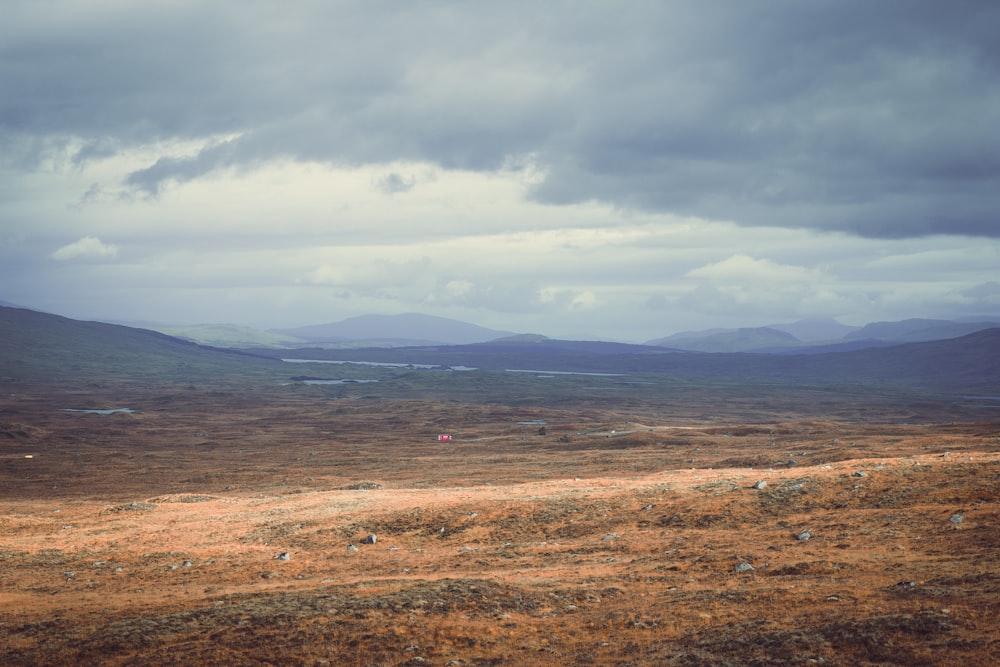 a field with mountains in the distance under a cloudy sky