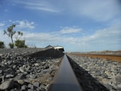 a train track with rocks and a building in the background