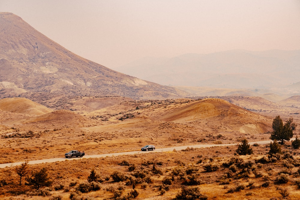 two cars driving down a dirt road in front of a mountain