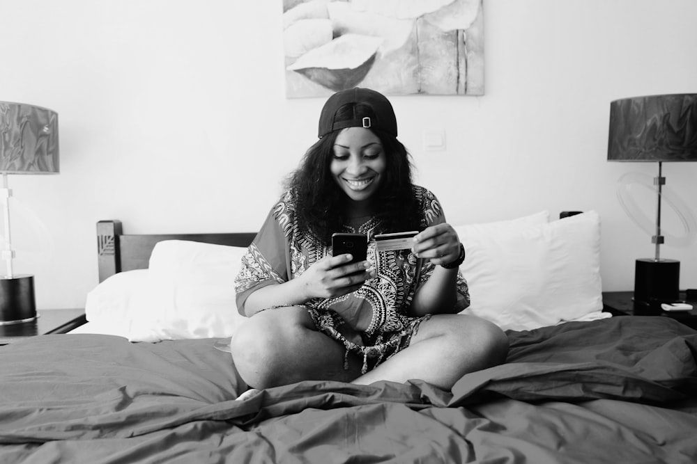 uma mulher sentada em uma cama olhando para seu telefone