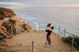 A couple embracing on a cliffside overlooking a sunset-drenched ocean horizon.