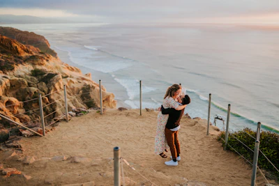 A couple embracing on a cliffside overlooking a sunset-drenched ocean horizon.