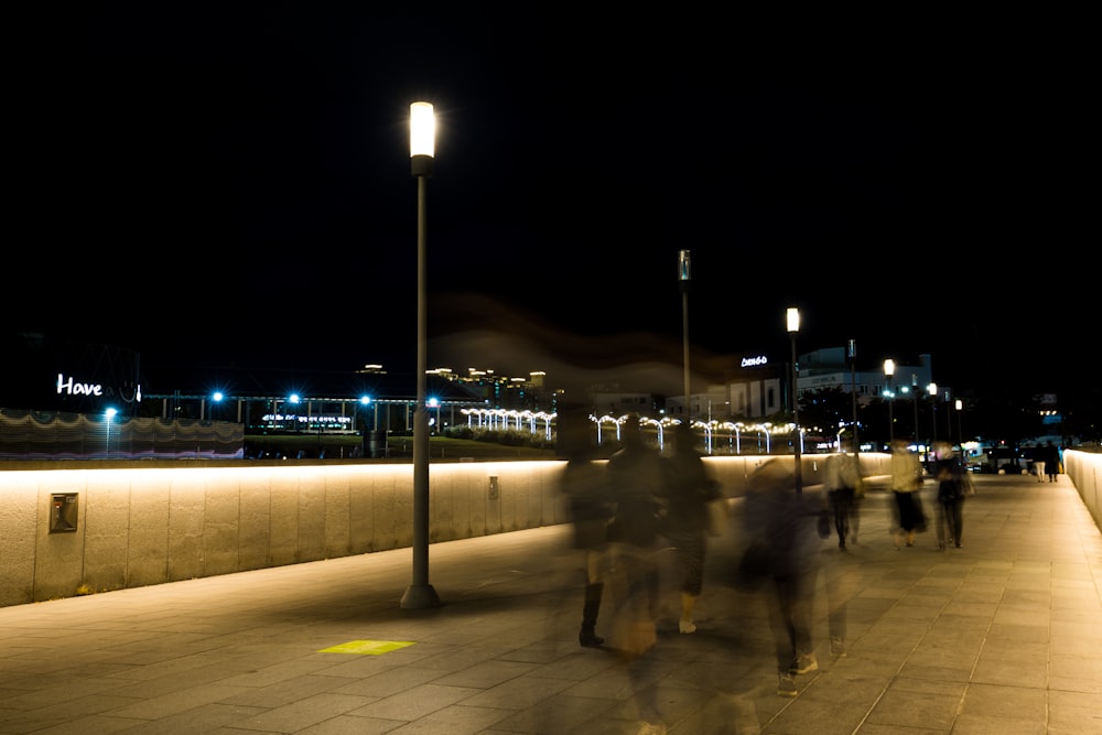 a group of people walking down a sidewalk at night