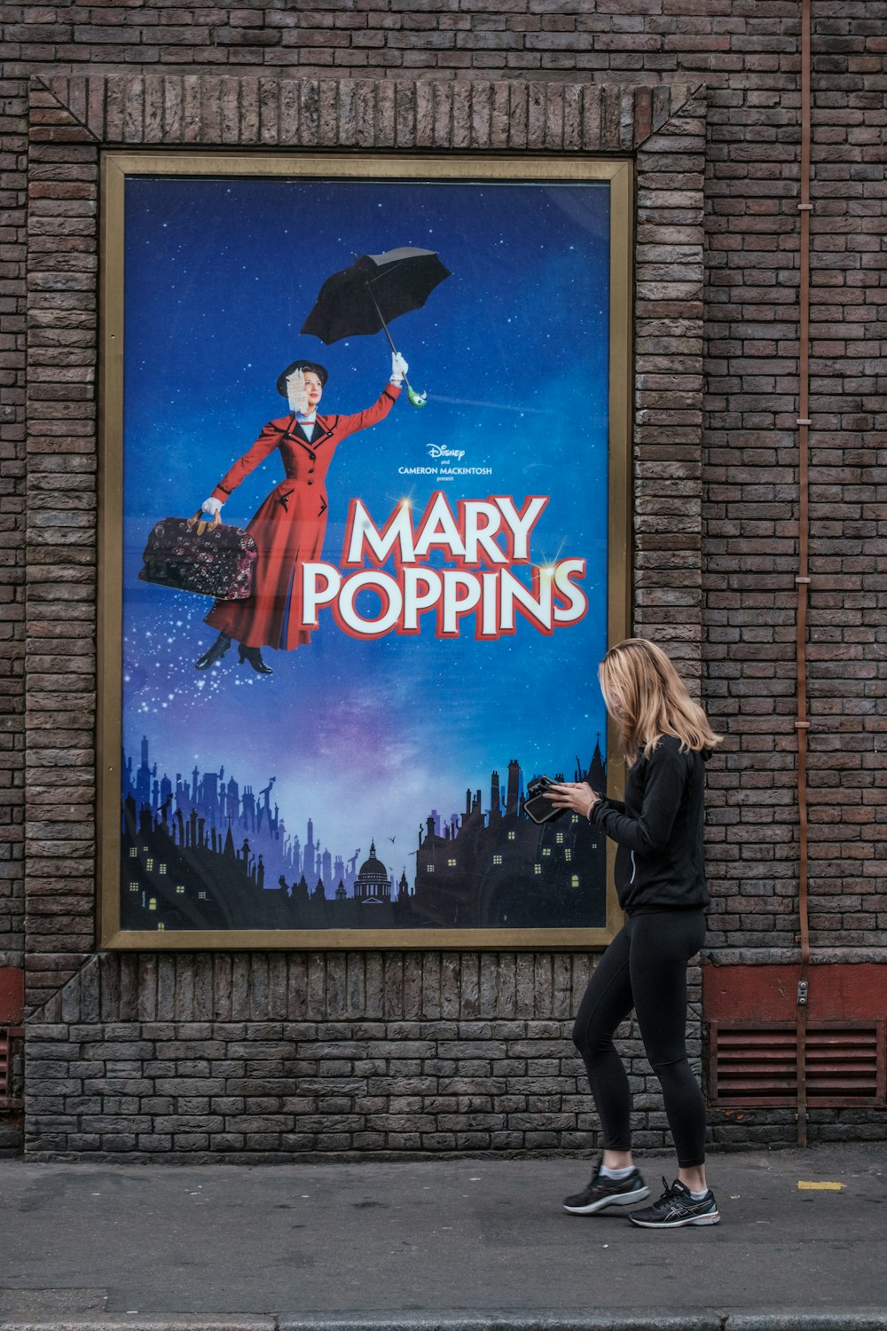a woman walking past a large poster of mary poppins